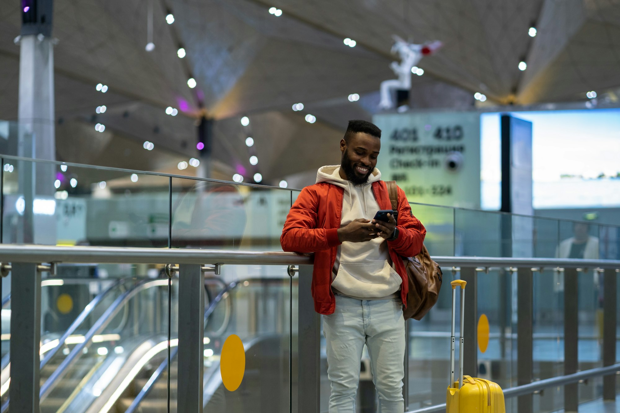 Young happy african traveler man using mobile phone, texting sms message after arrival in airport